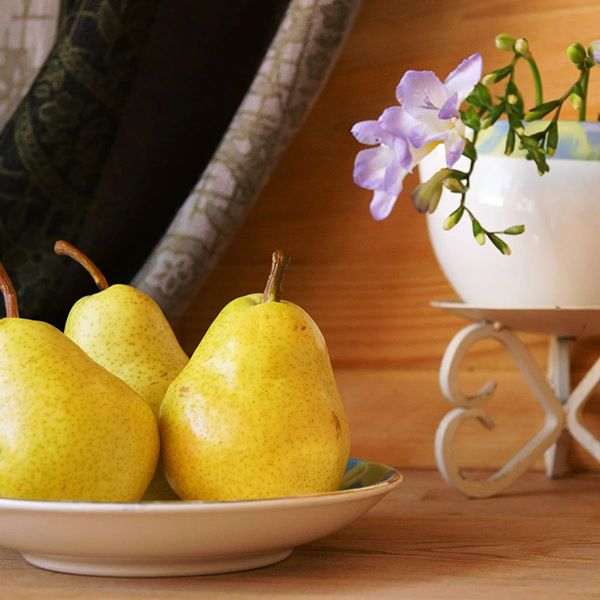 two pears on a plate with flower pot in background