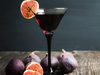 Red cocktail in a martini glass with figs on a wooden surface