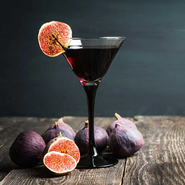 Red cocktail in a martini glass with figs on a wooden surface