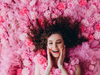 Woman surrounded by pink flowers with a joyful expression