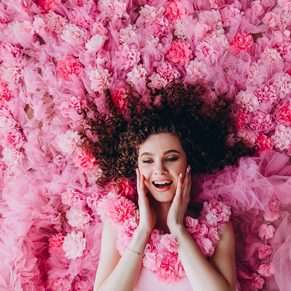 Woman surrounded by pink flowers with a joyful expression
