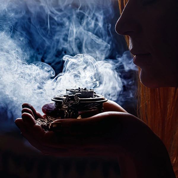 Person holding a small metal object with smoke rising, against a dark background