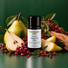Pepperberry Pear fragrance oil bottle with whole and sliced pears, clusters of red berries, green leaves and rough wood.
