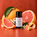 Pink Citron fragrance oil bottle with whole and sliced pink grapefruit, curled citrus peel, green leaves and white blossoms.