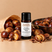 Roasted Chestnuts fragrance oil bottle with whole and split roasted chestnuts, a paper bag and a dark roasting pan.