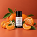 Sun Drenched Clementine fragrance oil bottle with whole and peeled clementines, citrus segments, curled peel and white blossoms.